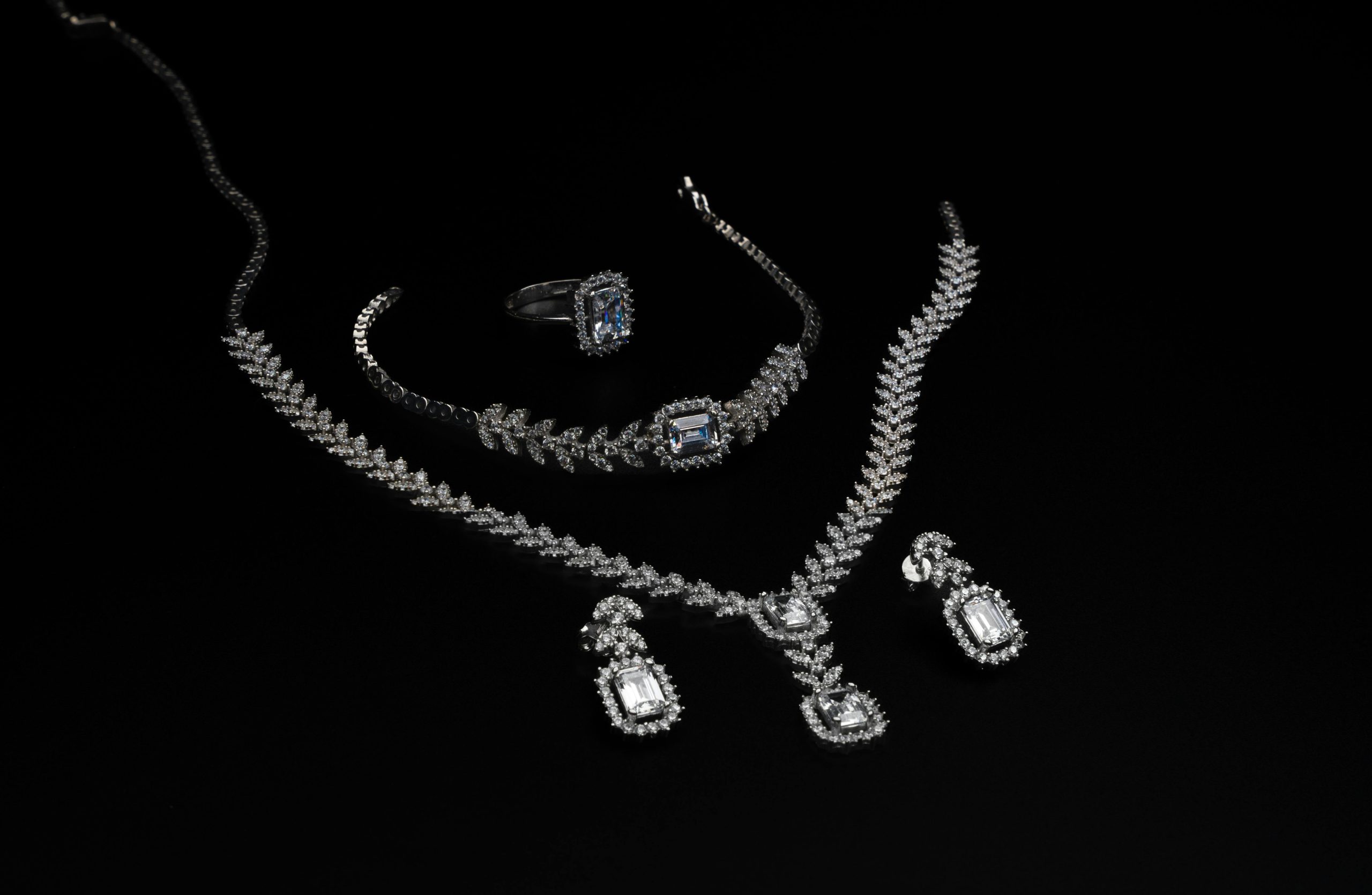 Elegant diamond jewelry set including necklace, bracelet, ring, and earrings on a black backdrop.